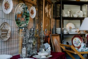 one wall of an antique booth shows an ornate metal clock and matching candlestitcks on a table with decorative plates hung on the wall behind it