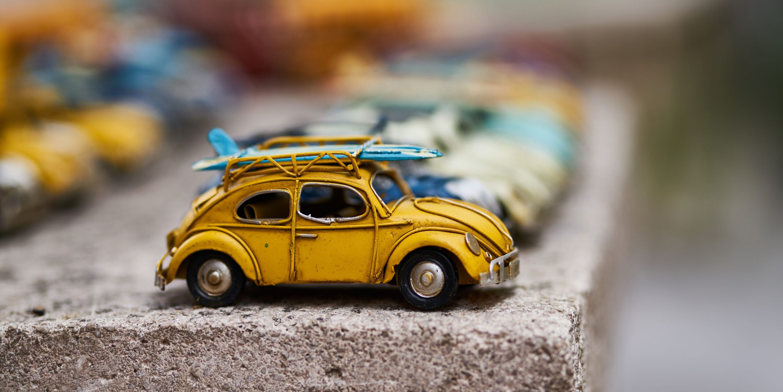 a vintage yellow toy car with a mini blue surfboard on top